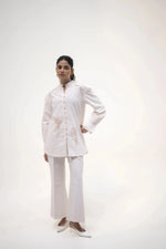 Load image into Gallery viewer, A model standing with a hand on her hip, wearing a long white shirt and white trousers, in a neutral pose against a soft background.
