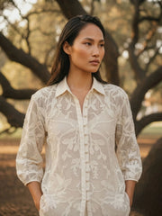 Woman wearing ivory openwork crochet summer lace shirt with floral embroidery, front close-up view, lightweight white lace blouse for women.